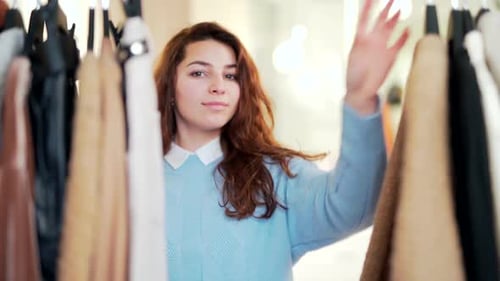 young attractive woman carefully examines clothes on a rack or hanger in a shopping center store.