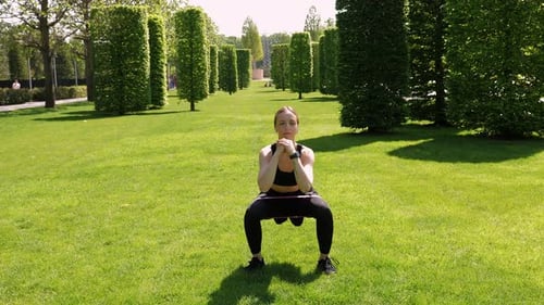 A Woman Trains Her Legs with Squats Using Rubber Bands for Fitness in a Park