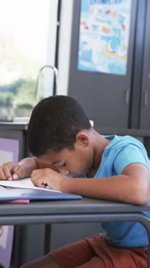 Vertical video: In school, boy resting head on desk, feeling tired in classroom