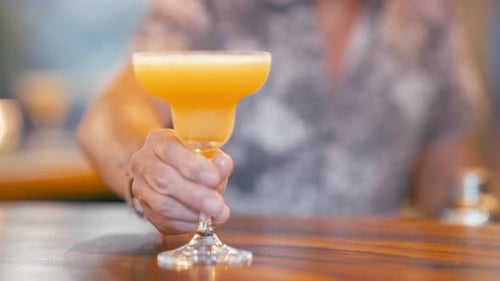 Bartender Holding Refreshing Orange Cocktail at Wooden Bar