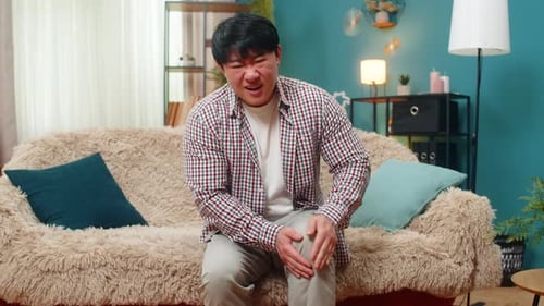 Adult Male Massaging Knee While Sitting on Sofa