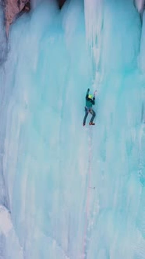 Mountaineer is Leading on Ice Ice Climbing on Frozen Waterfall Aerial View Vertical Video