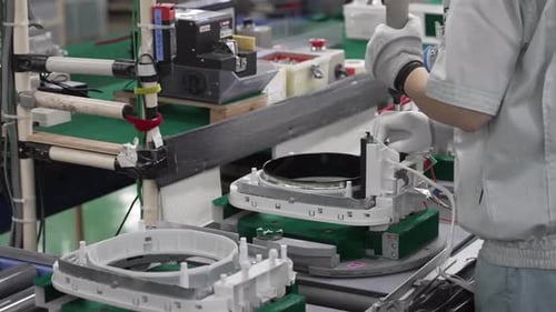 Ouvrier de montage manipulant un grand châssis de bobine d'induction IH avec éléments chauffants sur ceinture verte