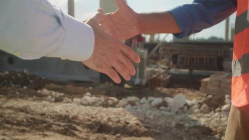 Closeup of Hands of Man in Yellow Vest and Man in White Shirt Shaking Hands on Blurred Background of