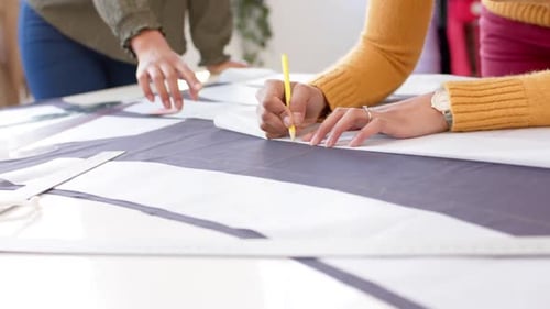 Diverse female fashion designers marking pieces of cloth from design patterns on table, slow motion