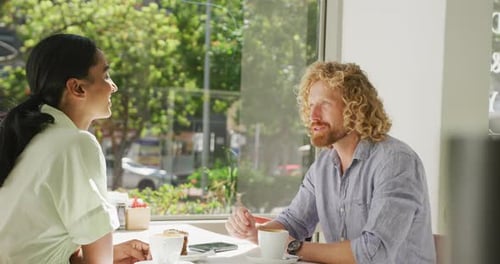 Happy diverse couple drinking coffee and talking at a table in cafe