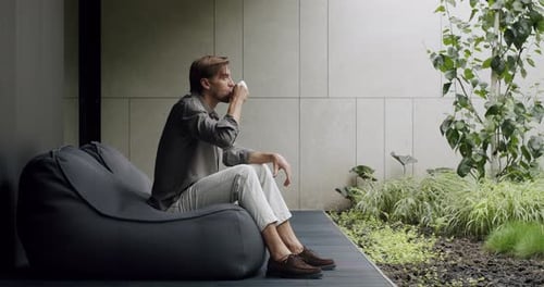 Man Sitting in Beanbag Chair Drinking Coffee Outside