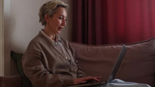 Side View of Serious Middleaged Homeowner Woman Using Financial Application on Laptop Counting