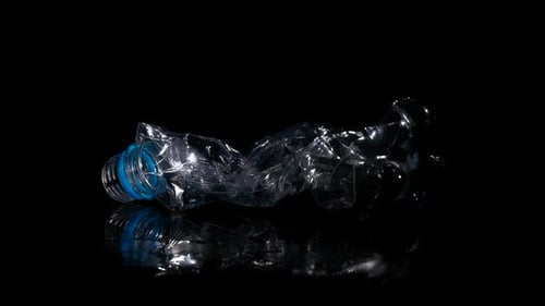 Squashed plastic bottle on dark reflective surface