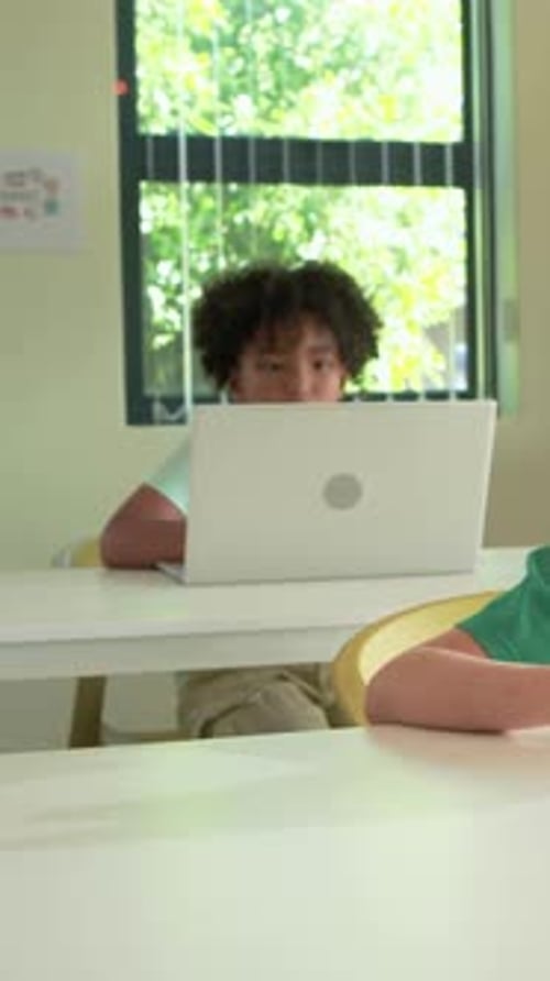 Vertical video: Screen drawing student forward, focusing on laptop in classroom, wearing mint tee