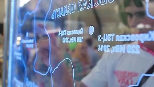 A Man Reviews a Map on a Computer Collaborating with Another on a Glass Wall
