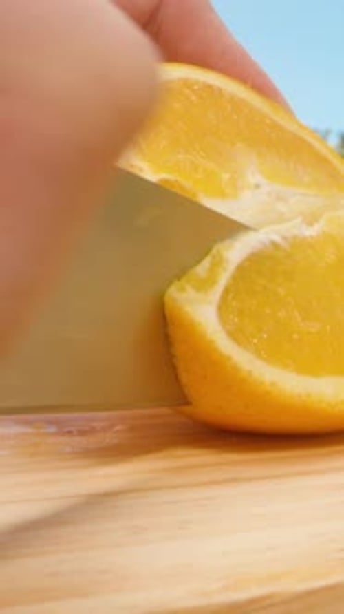 Vertikales Video. Messer schneiden frische Orangenspalten aus nächster Nähe auf Holzoberfläche im hellen Außenbereich