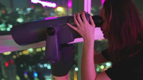 Young woman looks through rooftop tower viewer at night