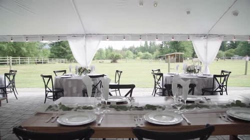 Elegant banquet tables for a luxurious outdoor wedding. Big tent, lot of opulence. Panning.