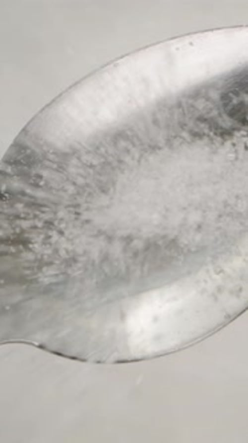 Vertical video. Sugar being poured into a spoon, top view, slow-motion.