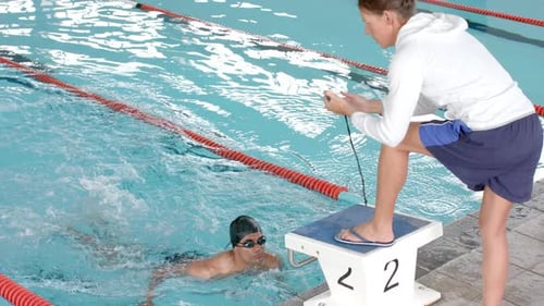 A Caucasian coach is timing a swimmer's lap