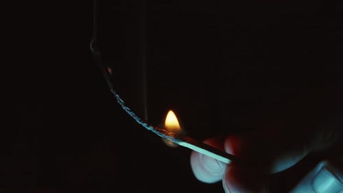 Fingers Holding a Burning Match Close Up in the Dark on a Black Background