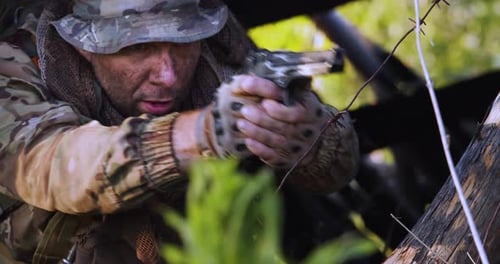 Man in Camouflage Aims Handgun from Woodland Bunker