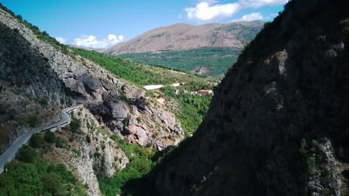 Flying Drone Over Mountains with Winding Mountain Road and Forest