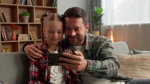 Father and Daughter Watching Smartphone on Couch