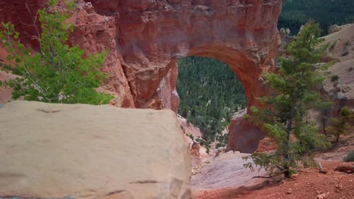 Plan panoramique lent avec une mise au point sur un support, depuis un rocher au premier plan jusqu'à une arche de hoodoo en grès à l'arrière