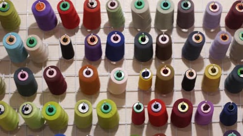 Farbige Garnrollen in verschiedenen Größen und Farben, die an der Wand von Tailor Workshop Fashion hängen