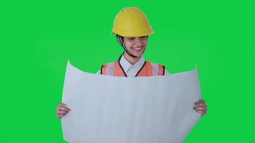 Happy Indian female architect looking through the blueprint Green screen