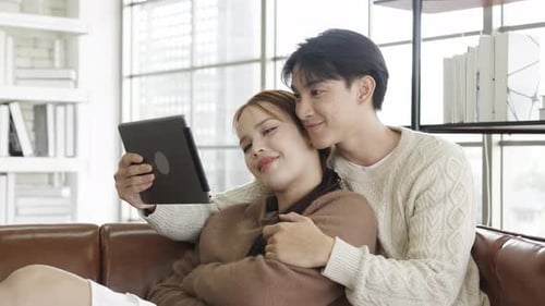 Smiling Couple Using Tablet on Couch Indoors