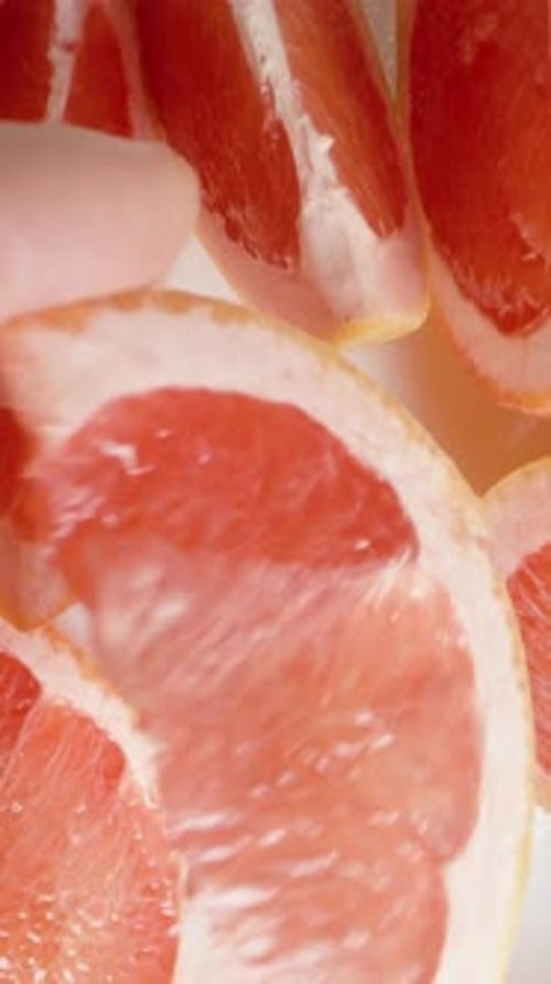 Vertical video. A man's hand takes a wedge of grapefruit and brings it close to the camera. Top view
