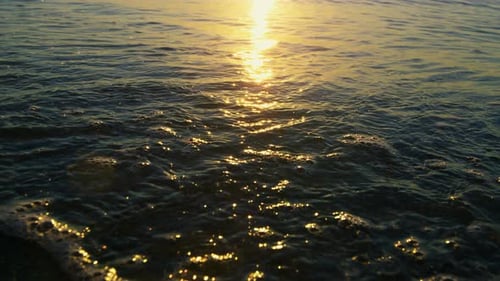 Reflejo de la luz del sol en las olas del mar que salpican la arena de la playa al amanecer dorado
