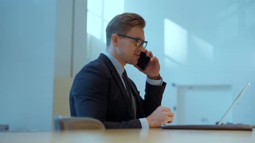 Smiling Man Using Laptop, Talking on Cellphone in Office