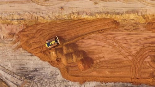 Aerial zoom in of bulldozer leveling land on construction site, top down view