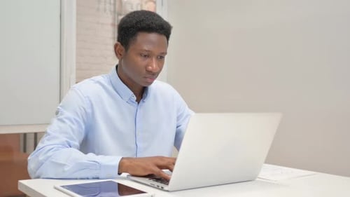 African Businessman Looking at Camera while Working on Laptop in Office