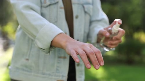 Woman spraying tick repellent onto hand in park, closeup