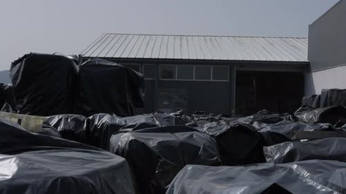 Large black plastic bags with recycling material stacked outside factory