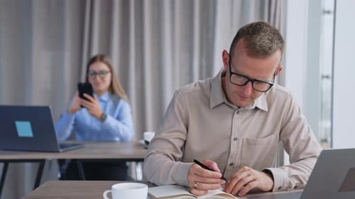 Ein vielbeschäftigter männlicher Angestellter mit Brille beugte seinen Kopf über das Notizbuch aus Papier.