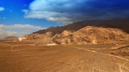 Hot plain desert limited by bare rocks. Huge cloudscape covering the mountain.