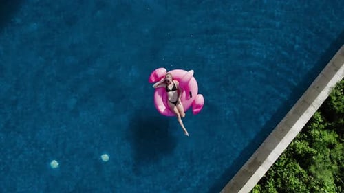 Happy Woman Sunbath and Dance in Infinity Pool with Inflatable Pink Flamingo
