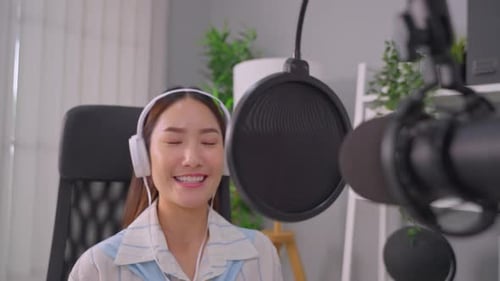Asian podcaster in headphones using microphone broadcasting in studio