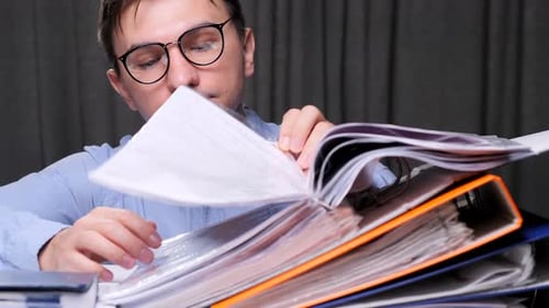 Accountant Searching Documents in Stack of Folders at Office Desk