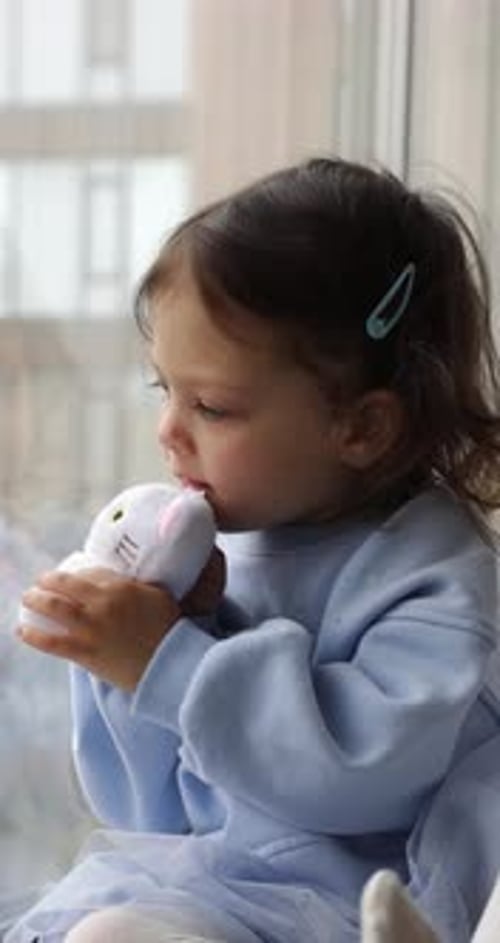 Young Child Sitting with Toy by Window
