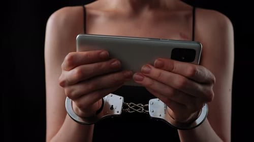 Woman with Handcuffs Holding a Smartphone in Low Light