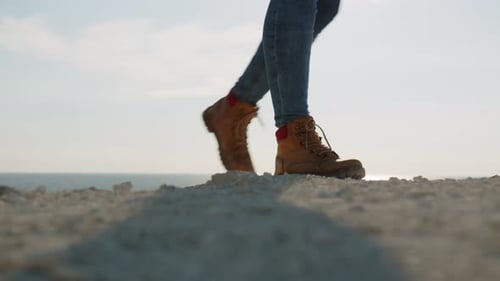 Women tourists climb to top of rocky shore passing against background of sky