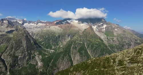 Drone shot of majestic alpine peaks with steep rocky cliffs, green valleys, and snow patches under