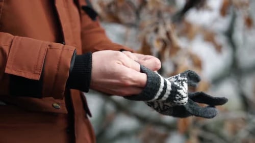 Man putting gray cotton glove with white patterns on his hand in forest on cold winter day, SLOW MOT