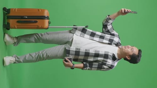 Full Body Of Asian Male Traveler With Luggage Having Video Call On Smartphone In The Green Screen