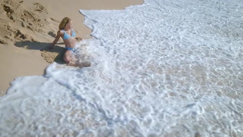Young woman in blue bikini sitting on ocean beach in tropical Paradise Island with turquoise water w