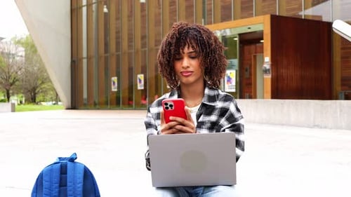 University Student Using Smartphone and Laptop on Campus