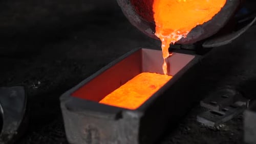 Slow motion foundry bucket pouring orange molten metal in cast with flaming sparks in a foundry