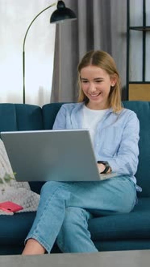 Smiling Woman Using Laptop on Couch in Living Room